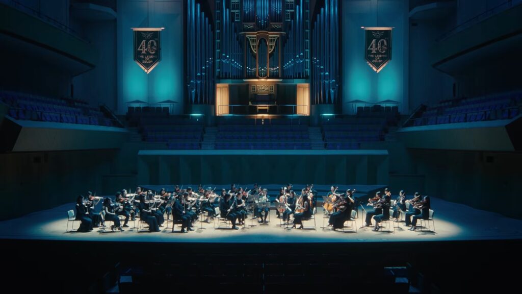 Orchestra performs the Zelda 40th Anniversary Triforce Medley beneath anniversary banners and a pipe organ.