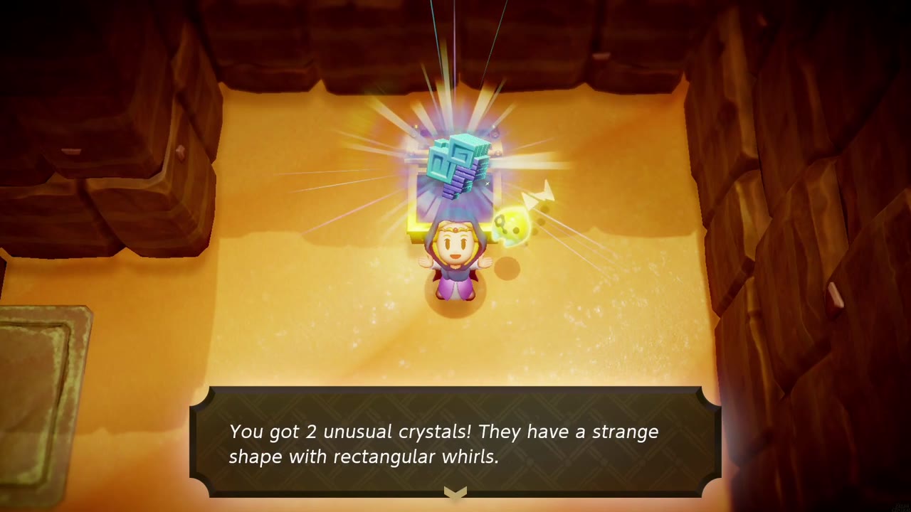 Zelda holds up 2 unusual crystals over an opened chest in a sandy, walled cave room in Gerudo Desert