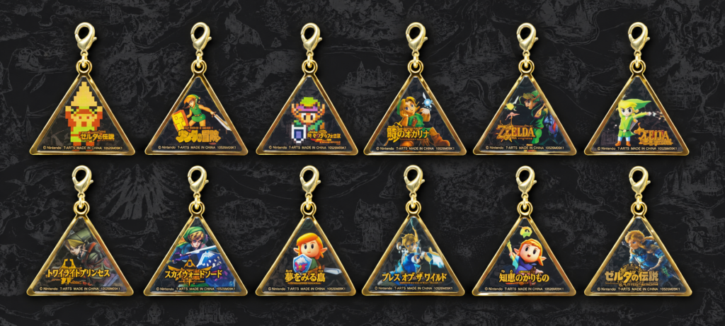 Twelve gold Triforce-shaped Zelda Historical Charm+ charms arranged in two rows, featuring artwork from The Legend of Zelda through Echoes of Wisdom.