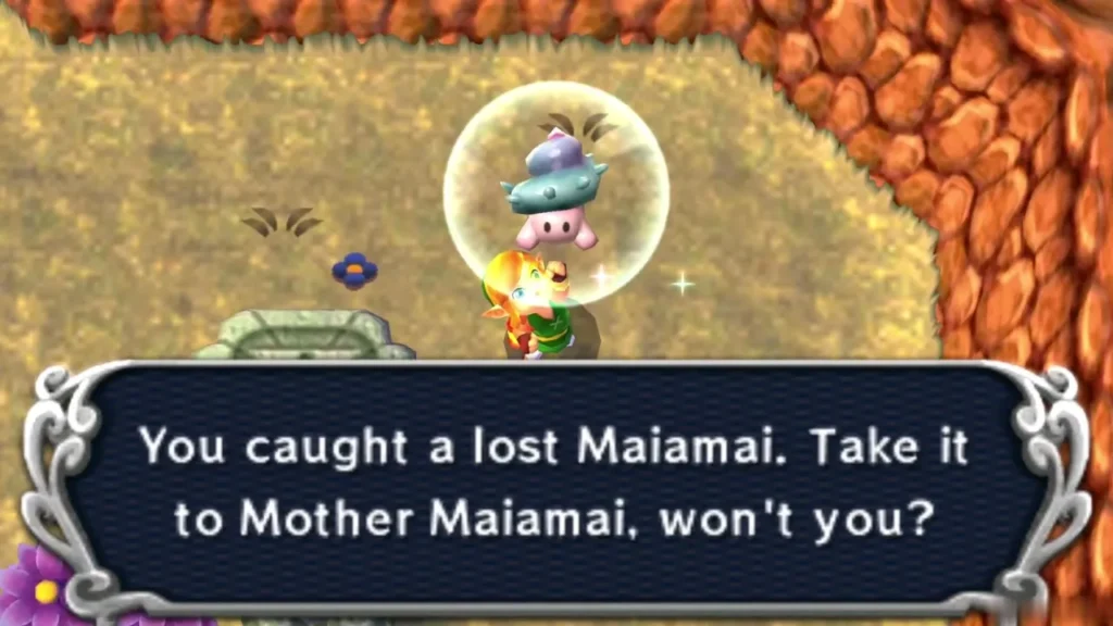 Link holding up a caught lost Maiamai in a bubble on a sandy ledge below a cobbled cliff, the catch message complete Link holding up a caught lost Maiamai in a bubble on a sandy ledge below a cobbled cliff, the catch message complete