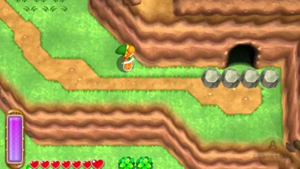 A row of grey boulders blocks a cave mouth on a red-earth path, with Link standing on the grass nearby A row of grey boulders blocks a cave mouth on a red-earth path, with Link standing on the grass nearby