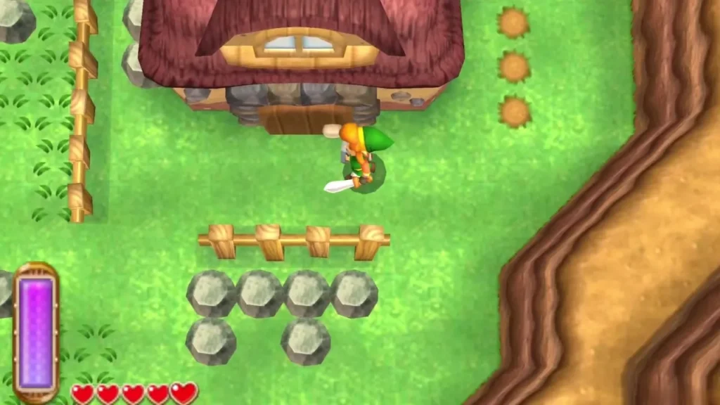 Link at the door of the Miner's House, with a row of grey rocks and a wooden fence in front of it Link at the door of the Miner's House, with a row of grey rocks and a wooden fence in front of it