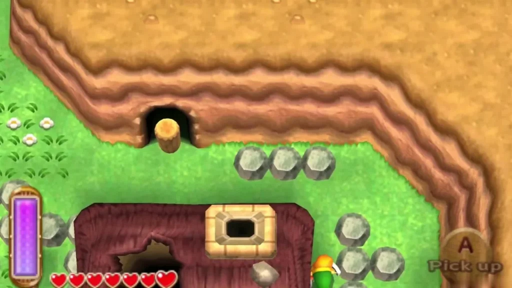 Pick Up prompt beside a row of grey rocks and a cave mouth on the red path, with Link ready to lift one Pick Up prompt beside a row of grey rocks and a cave mouth on the red path, with Link ready to lift one
