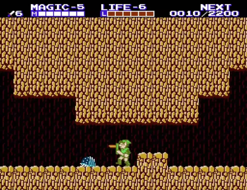 Link in a sandstone cave with brown walls and a sand floor, a blue enemy at the bottom left