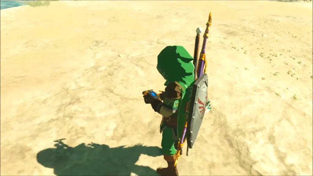 Link holding the Sheikah Slate on the sand beside the water Link holding the Sheikah Slate on the sand beside the water