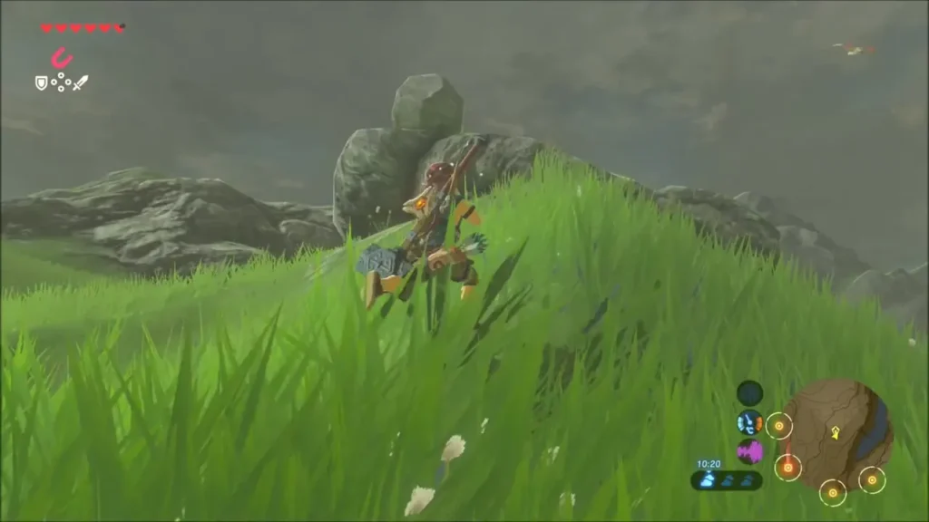 Link climbing the grassy ridge toward a pile of boulders with a round rock on top