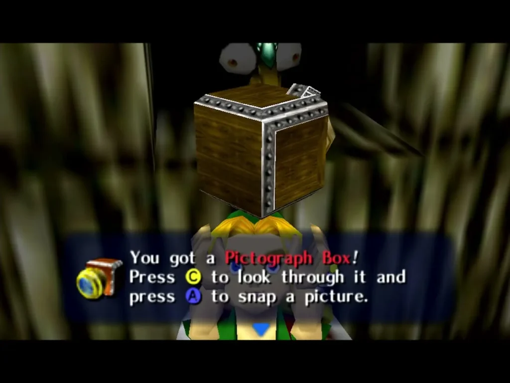 Link holds up the Pictograph Box, the box saying to press C to look through it and A to snap a picture Link holds up the Pictograph Box, the box saying to press C to look through it and A to snap a picture