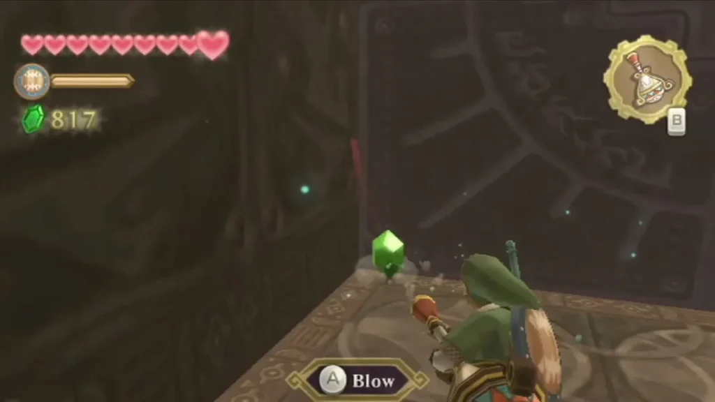 Link aims the Gust Bellows at a green gem on the ground and the Blow prompt appears. Link aims the Gust Bellows at a green gem on the ground and the Blow prompt appears.
