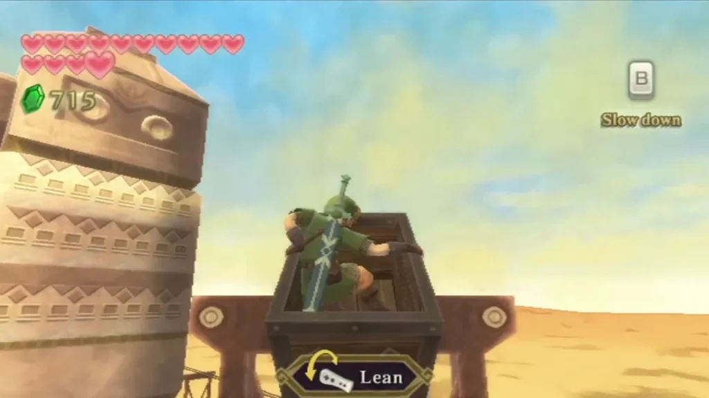 Link leans in a mine cart on the sand track beside a stone pillar, with a Slow down prompt. Link leans in a mine cart on the sand track beside a stone pillar, with a Slow down prompt.