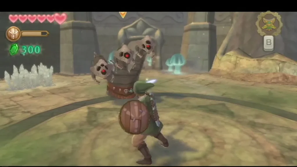 The three-headed Staldra rears up in the sand arena with its heads raised while Link stands ready with his shield. The three-headed Staldra rears up in the sand arena with its heads raised while Link stands ready with his shield.